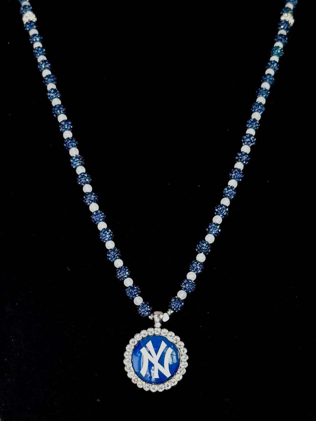 A beaded necklace featuring a blue and white New York Yankees logo pendant, displayed against a solid black background.