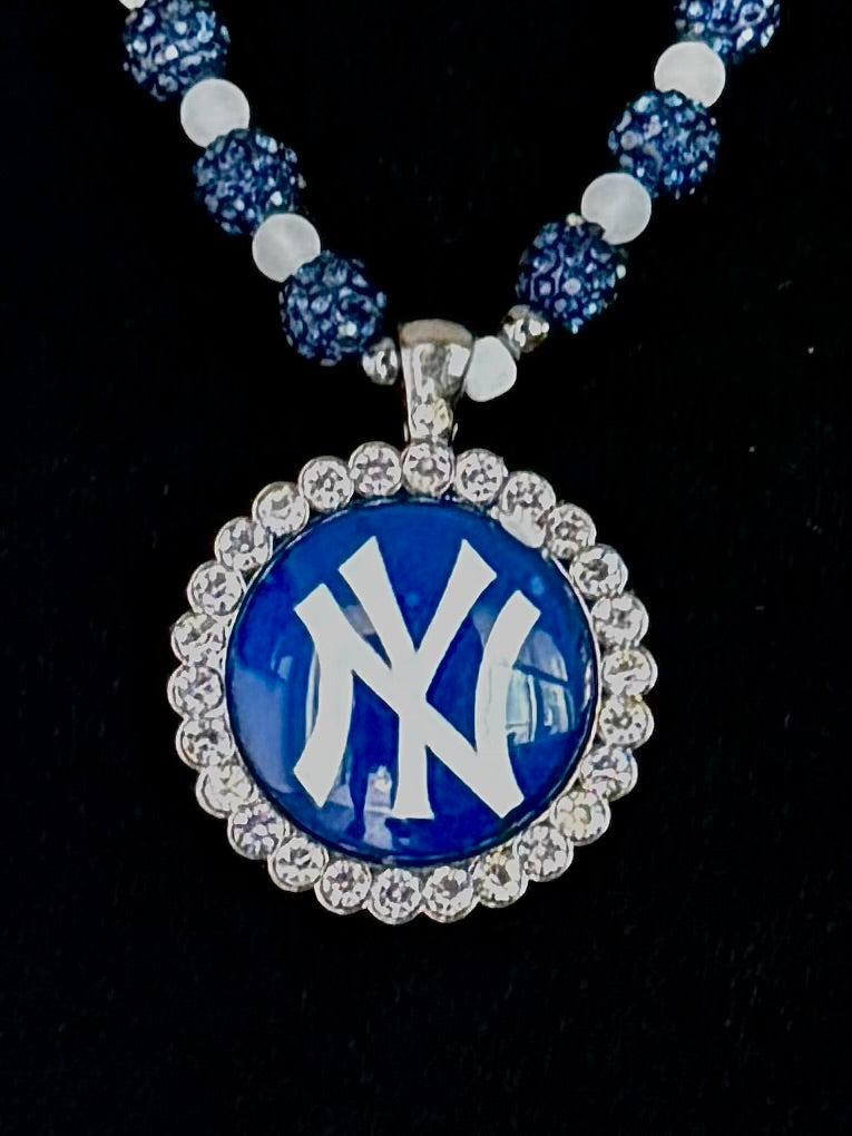 A beaded necklace featuring a round pendant with the New York Yankees logo in blue and white, surrounded by a silver-tone rhinestone halo, on a black background.